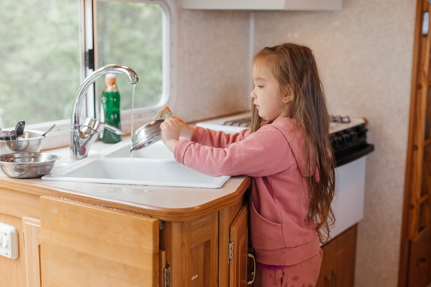 Little girl washing dishes in the kitchen of a travel trailer