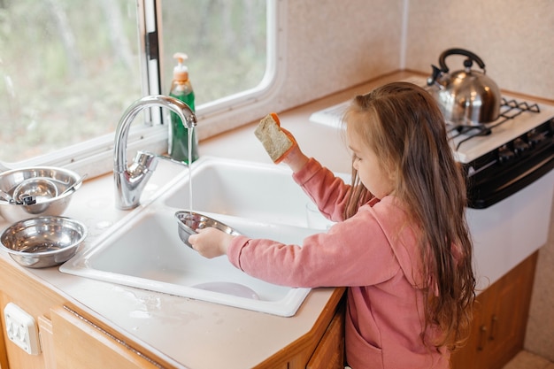 Little girl washing dishes in the kitchen of a travel trailer