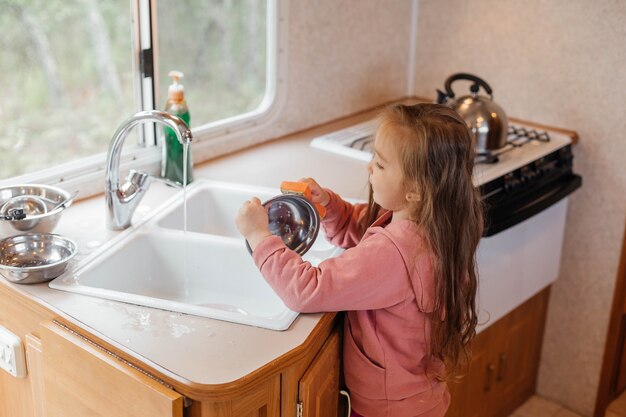 Little girl washing dishes in the kitchen of a travel trailer