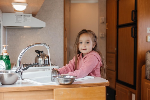 Little girl washing dishes in the kitchen of a travel trailer