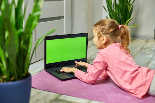 Little girl watching online video on laptop and doing stretching fitness exercises at home