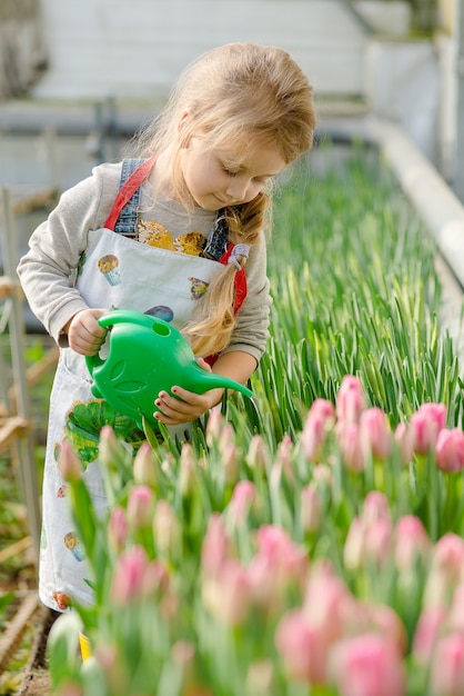 Little girl watering flowers in a greenhouse in spring.