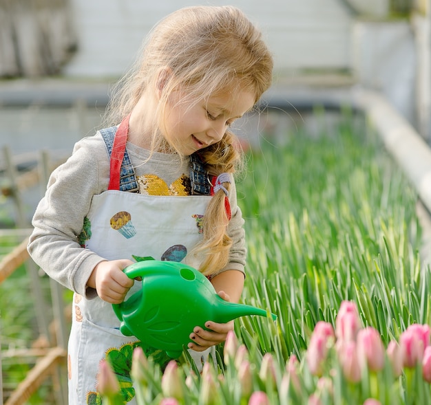 Little girl watering flowers in a greenhouse in spring.