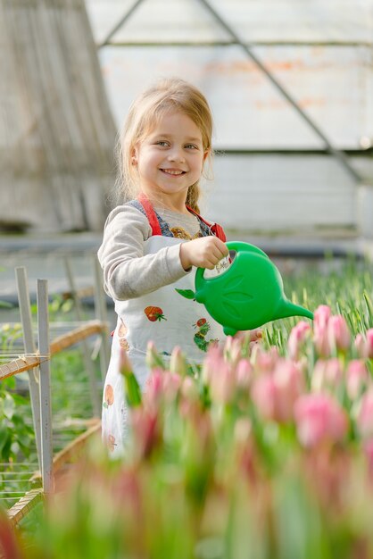 Little girl watering flowers in a greenhouse in spring.