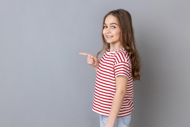 Little girl wearing pointing aside at empty place for ad content and expressing happiness