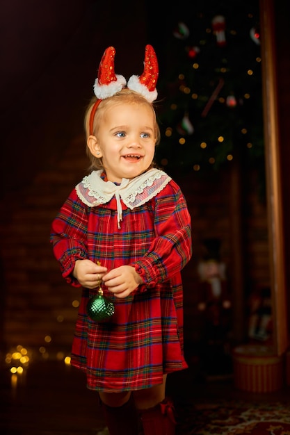 Little girl wearing santa suit and red horns against white background