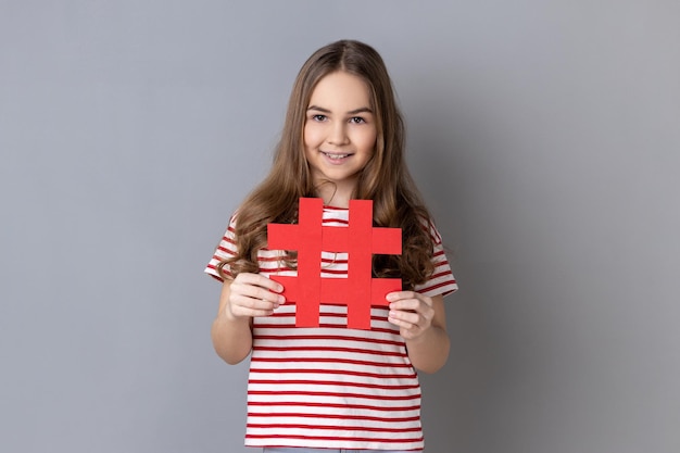 Little girl wearing striped Tshirt holding hashtag symbol promoting viral topic in social network