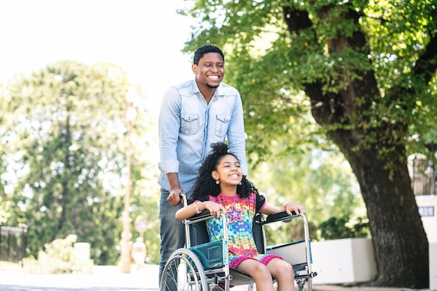 A little girl in a wheelchair enjoying and having fun with her father while on a walk together outdoors