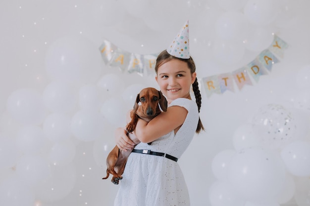 Little girl in a white dress with her beloved dog dachshund in her arms celebrates her birthday