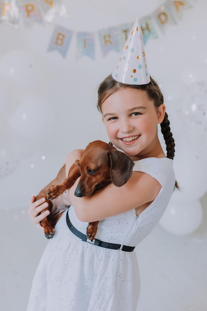 Little girl in a white dress with her beloved dog dachshund in her arms celebrates her birthday