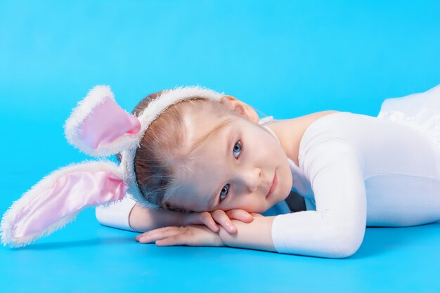 Little girl in a white rabbit costume on a blue wall. The baby lies dreaming on the floor.