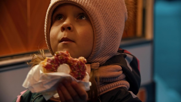 A little girl in winter clothes eating donut outdoors