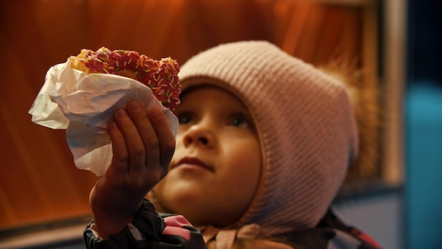 A little girl in winter clothes hands up a donut