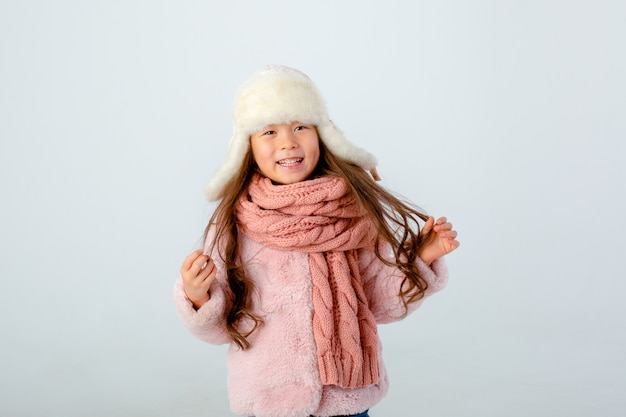 A little girl in a winter hat and scarf is isolated on a white background