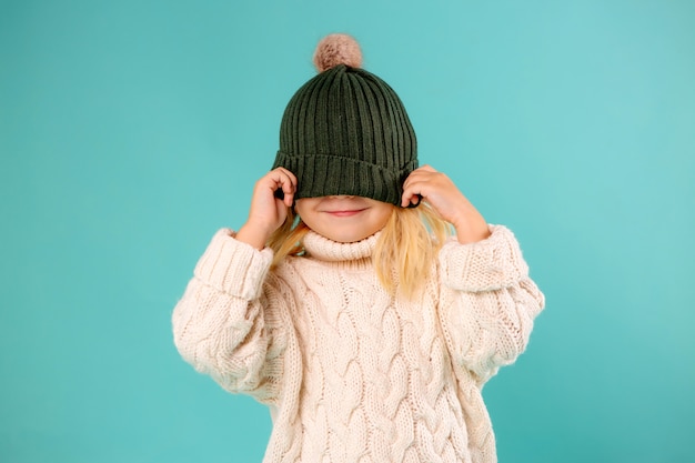 little girl in winter hat and sweater on blue  