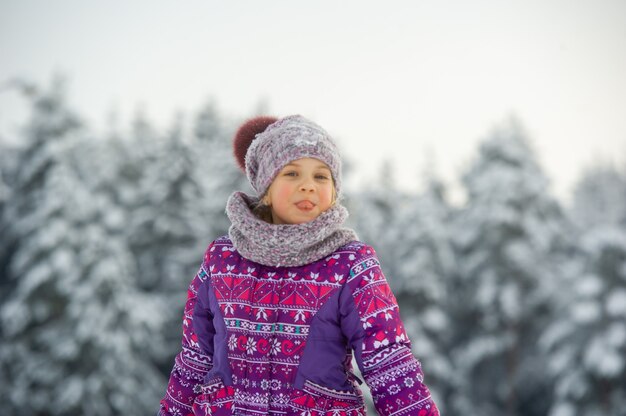 A little girl in winter in purple clothes walks through a snow-covered forest