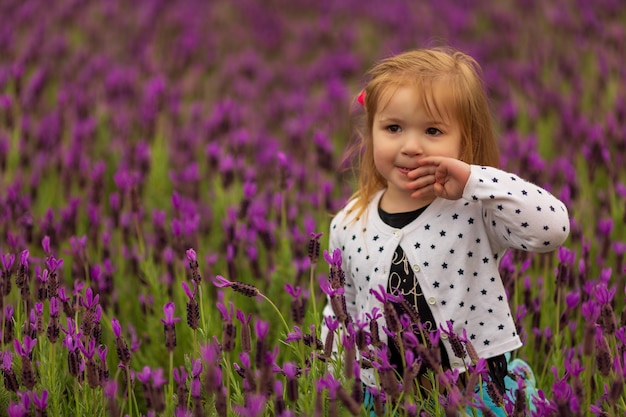 Little girl wiping the mouth and looking away while standing in field of wild violet flowers in coun...