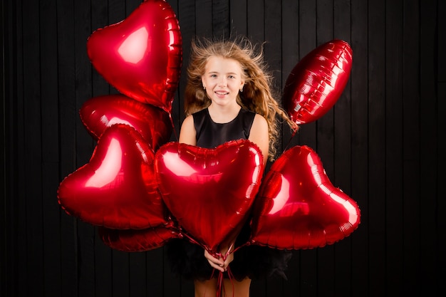 A little girl with balloons in the form of a heart send a kiss on a black background