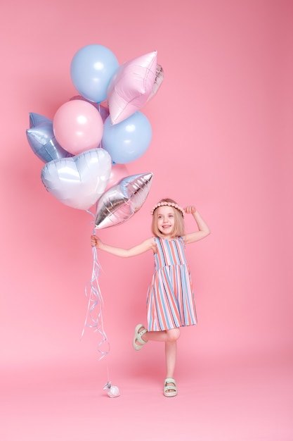 Little girl with balloons on a pink surface