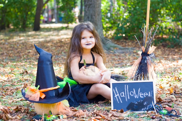 A little girl with black hair in a witch costume with a broom in her hands.