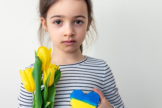 Little girl with a bouquet of tulips and a heart with the flag of ukraine