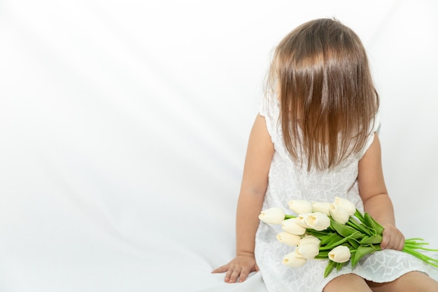 Little girl with a bouquet of tulips in a white dress  looks to the side a gentle smile