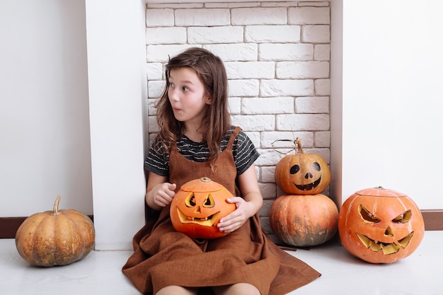 Little girl with carved pumpkin on Halloween at home sitting next to fireplace