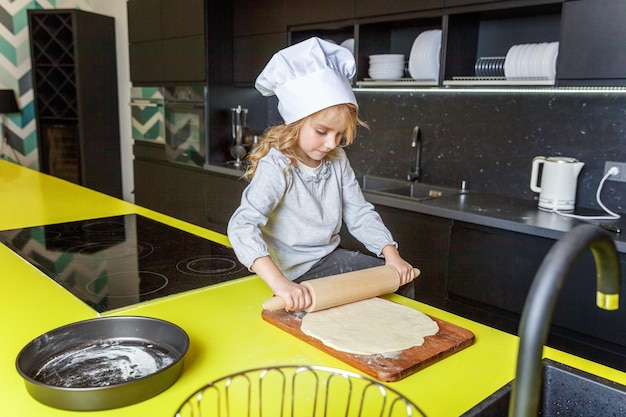 Little girl with chef hat rolling pin preparing dough bake homemade holiday apple pie in kitchen kid