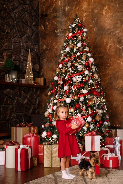 A little girl with Christmas gifts and a dog near a large Christmas tree. New Year. Christmas. postcard