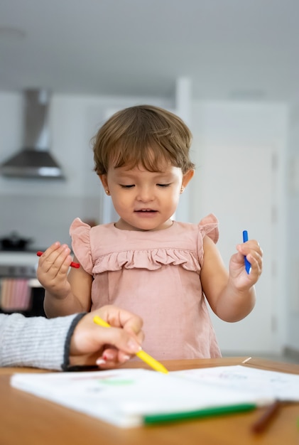 little girl with colored crayons while painting at home