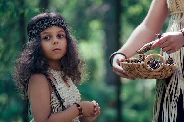 A little girl with dark curly hair dressed as a native in the forest collects bumps with her mother