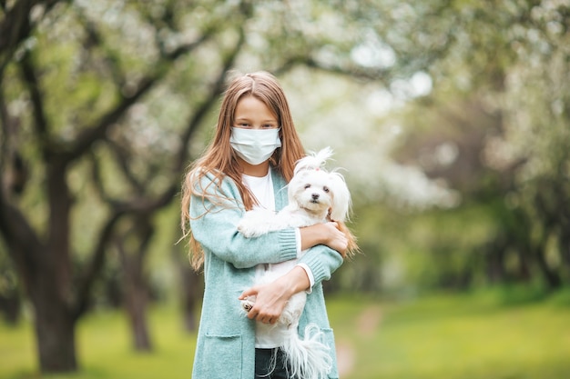 Little girl with dog wearing protective medical mask for prevent virus outdoors in the park