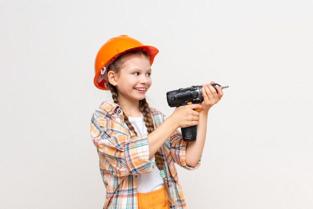 A little girl with a drill and wearing a protective construction helmet depicts a builder on a white isolated background The concept of repair