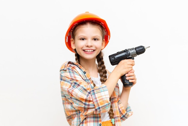 A little girl with a drill and wearing a protective construction helmet depicts a builder on a white isolated background The concept of repair