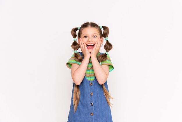 A little girl with a fashionable hairstyle and long hair holds her cheeks and smiles broadly