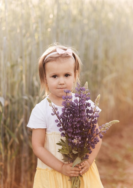 Little girl with flowers in the fieldThe baby is holding a bouquet of lupines in her handsA child in the middle of a field collects a bouquet of flowers