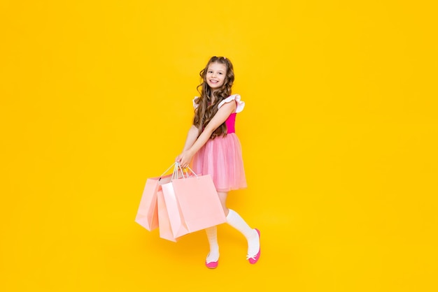 A little girl with fulllength shopping A fashionista after shopping on a yellow isolated background Children's sale The young princess is happy to make new purchases