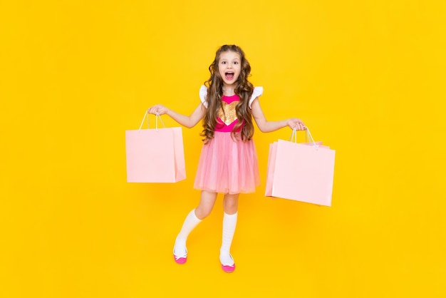 A little girl with fulllength shopping A fashionista after shopping on a yellow isolated background Children's sale The young princess is happy to make new purchases