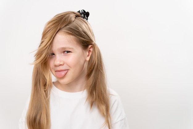 Little girl with funny collected hair and tongue stuck out on a white background. children's haircuts and hairstyles. shampoo and cosmetics for children. copy space