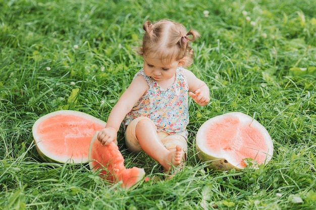 little girl with a funny hairstyle eats a watermelon on the lawn in the park healthy snack for kids