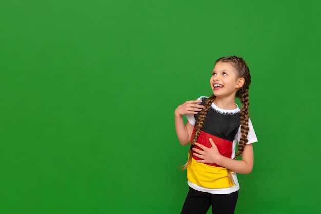 A little girl with a German flag on her Tshirt looks at your advertisement on a green isolated background German language courses for schoolchildren Copy space