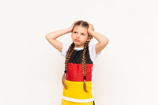 A little girl with a German flag on a Tshirt with long hair braided into pigtails clutching her gulova with two hands on a white isolated background Language courses