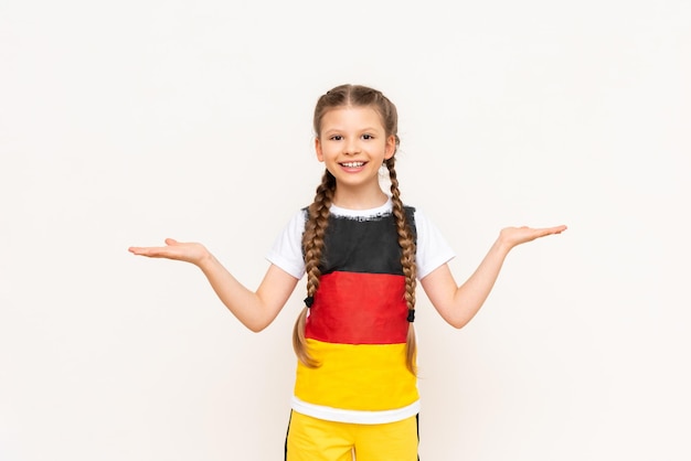 A little girl with a German flag on a Tshirt with long hair in pigtails holds your advertisement on a white isolated background on her palms Language courses Copy space