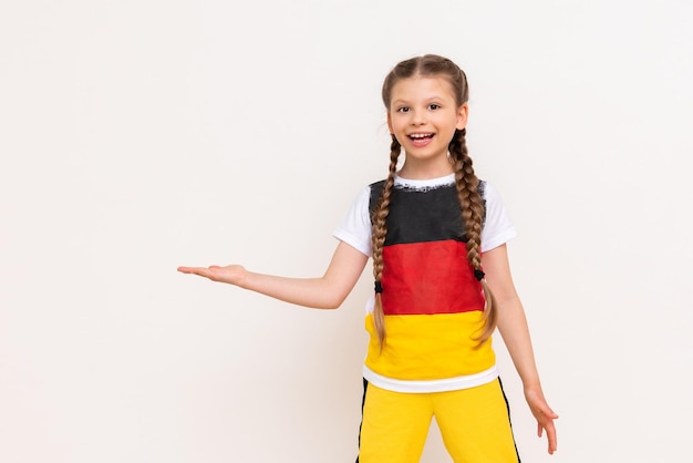 A little girl with a German flag on a Tshirt with long hair in pigtails holds your advertisement on a white isolated background on her palms Language courses Copy space