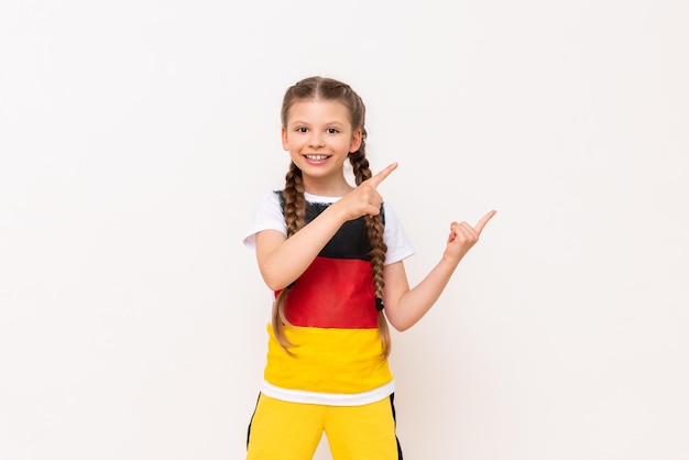 A little girl with a German flag on a Tshirt with long hair in pigtails points up with her index finger sideways at your advertisement on a white isolated background Language courses