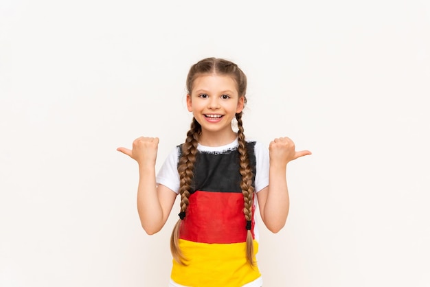 A little girl with a German flag on a Tshirt with long hair in pigtails points up with her index finger sideways at your advertisement on a white isolated background Language courses