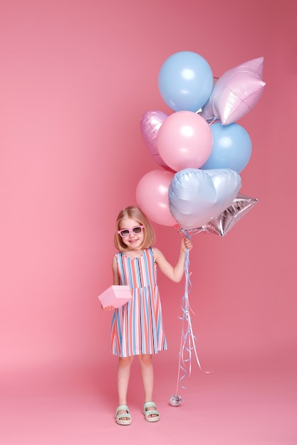 Little girl with a gift and balloons on a pink surface