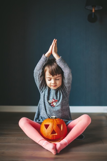 Little girl with a Halloween pumpkin sitting in a lotus position