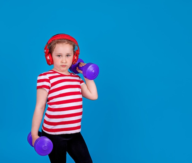 A little girl with headphones is doing sports with dumbbells in her hands