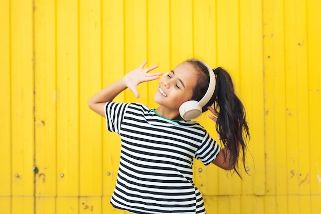 a little girl with headphones listening to music a child is dancing on the background of a yellow fe